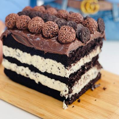 Um pedaço robusto de um delicioso slice cake com brigadeiros em cima e várias camadas de recheio