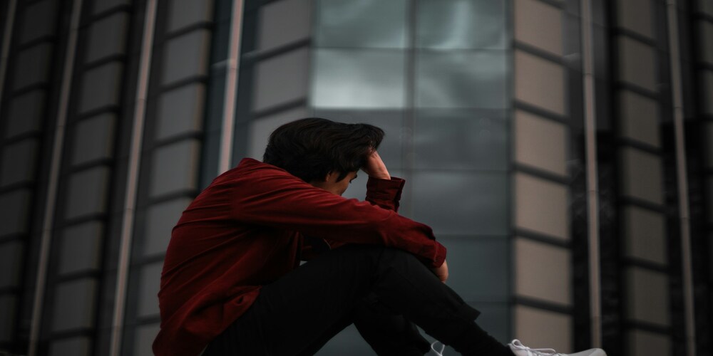 Um homem sentado com a mão na cabeça pensando demais, e como essa relação pode prejudicar a tomada de decisão